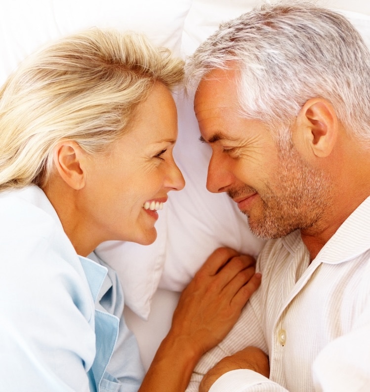 Smiling romantic mature couple holding hands on bed